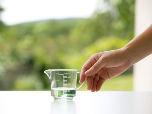 One hand reaches for a small measuring cup filled with Frosch sensitive detergent aloe vera