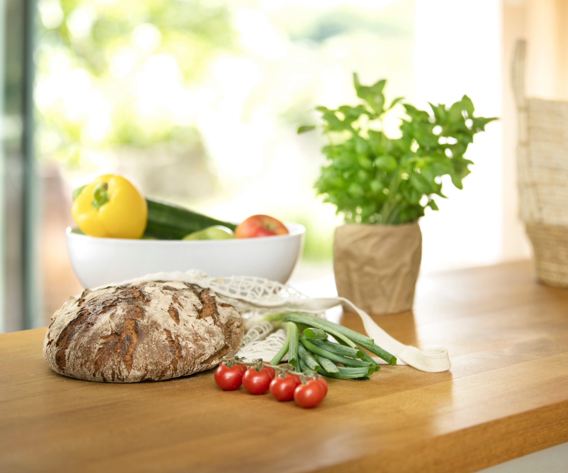 Bread, tomatoes, basil and a bowl with vegetables on a wooden table